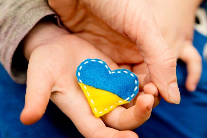 Ukraine flag theme. Heart shape pin badge made of blue and yellow stuffed felt in child hand. Topical issues of war. Freedom fighters. Support of nations, unity